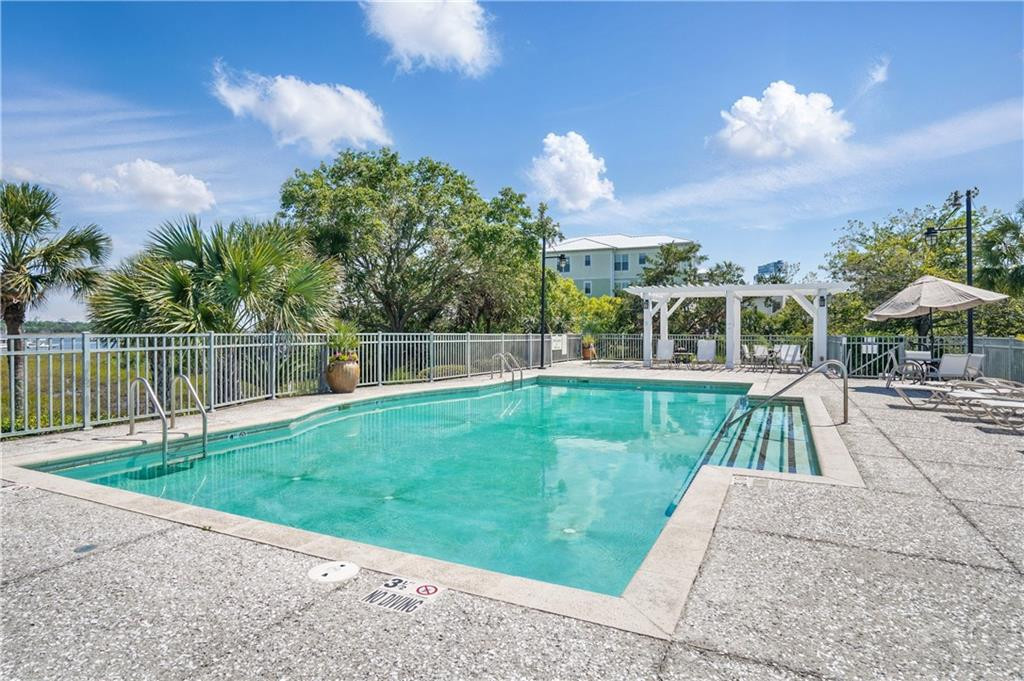 Outdoor pool with a white pergola, palm trees, and lounge chairs beside the fenced deck.