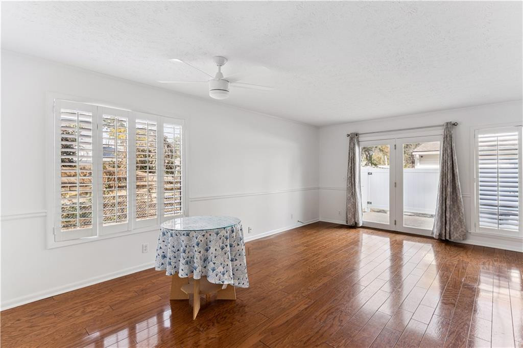 Bright room with polished hardwood floors, plantation shutters, and French doors opening to a fenced area.