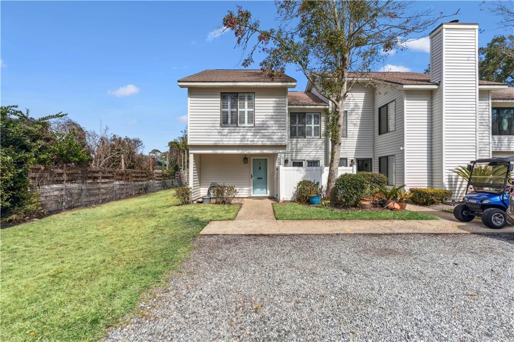 White two-story townhouse with a teal front door, lawn, and golf cart beside the gravel driveway.