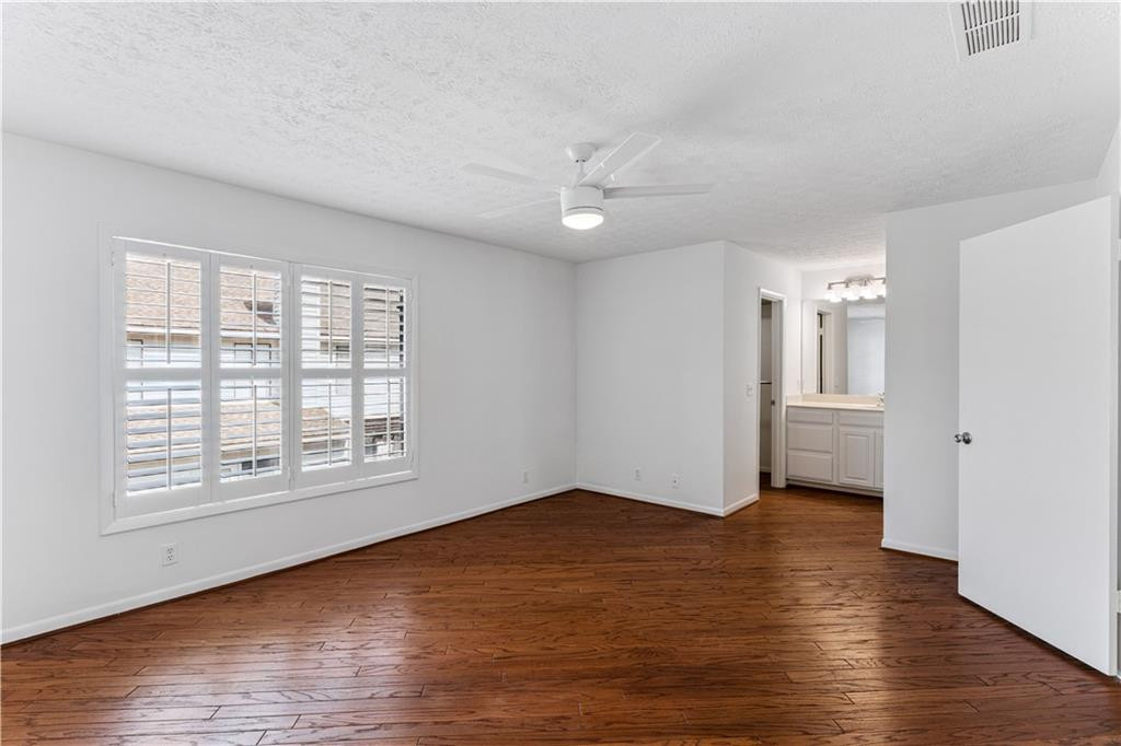 Empty room with hardwood floors, plantation shutters, and a ceiling fan.