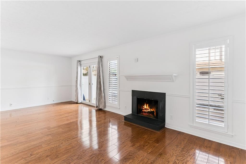 Empty living room with a lit fireplace, glossy hardwood floors, and shuttered windows.