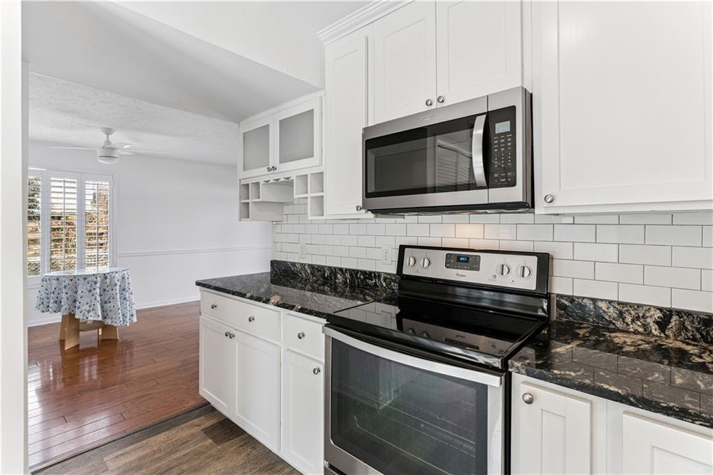 White kitchen with dark granite counters, subway tile backsplash, and stainless-steel appliances.