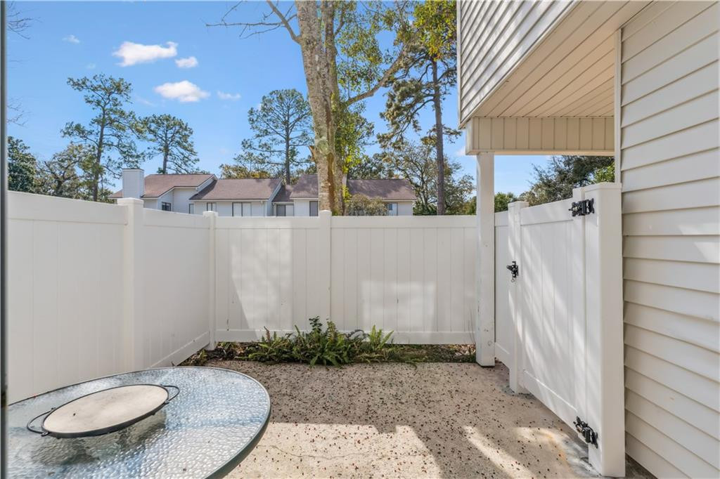 Fenced patio beside a light-colored house with a round glass-top table and gravel ground.