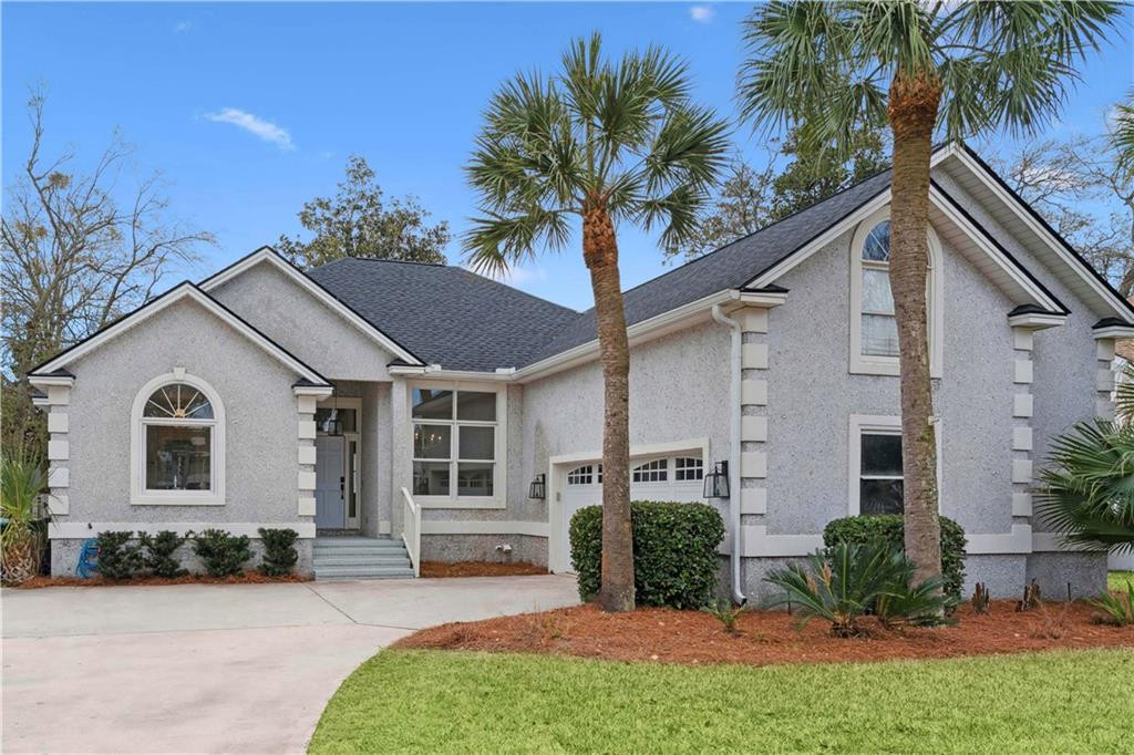 Light-gray stucco house with arched windows, an attached garage, and palm trees by the driveway.