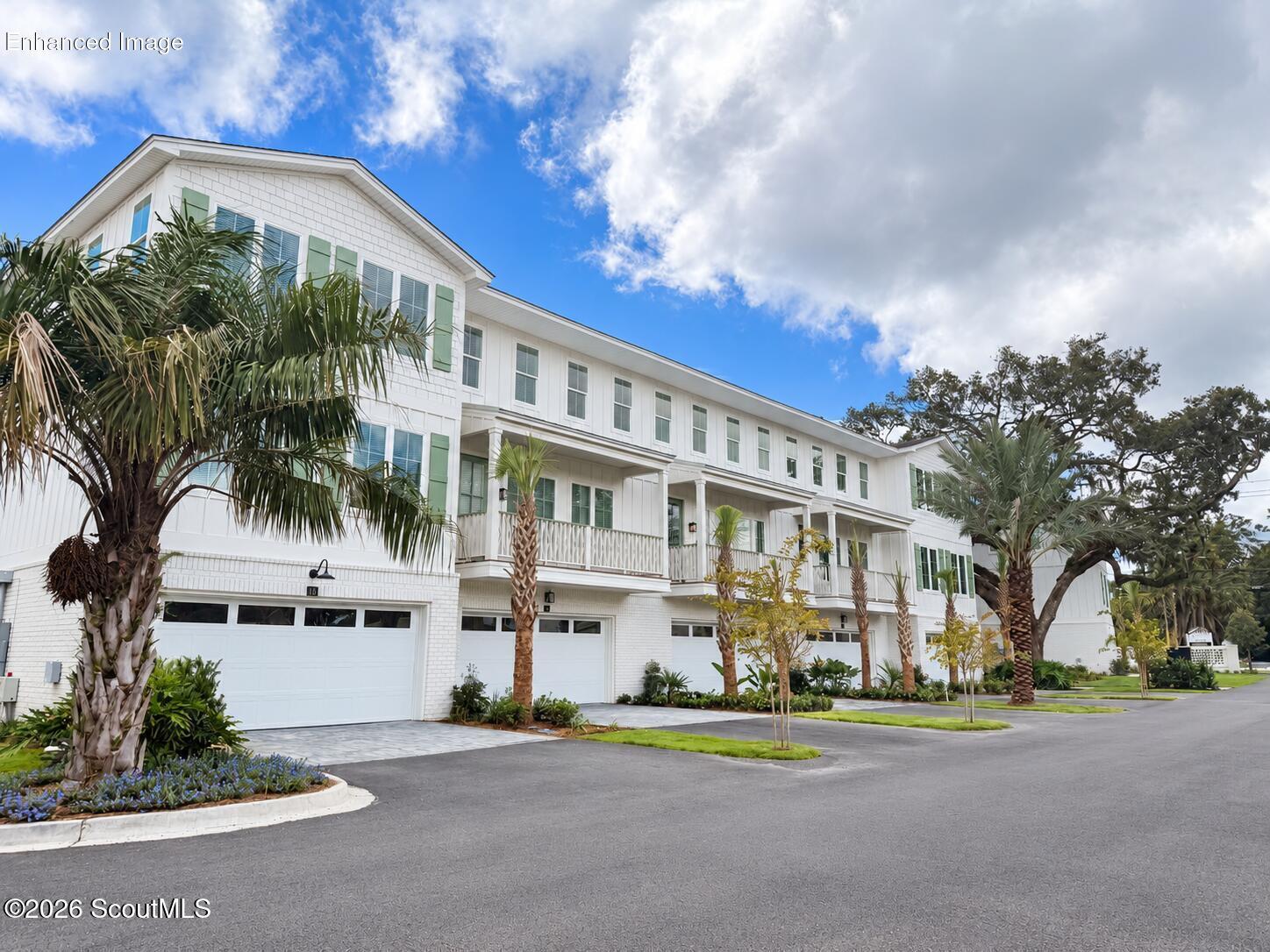 White multi-story townhomes with green shutters, balconies, garage doors, and palm trees.