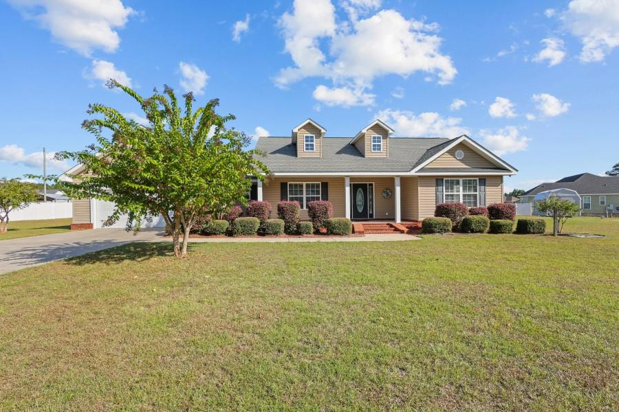 Tan single-story home with two roof dormers, a covered entry, and a broad front lawn.