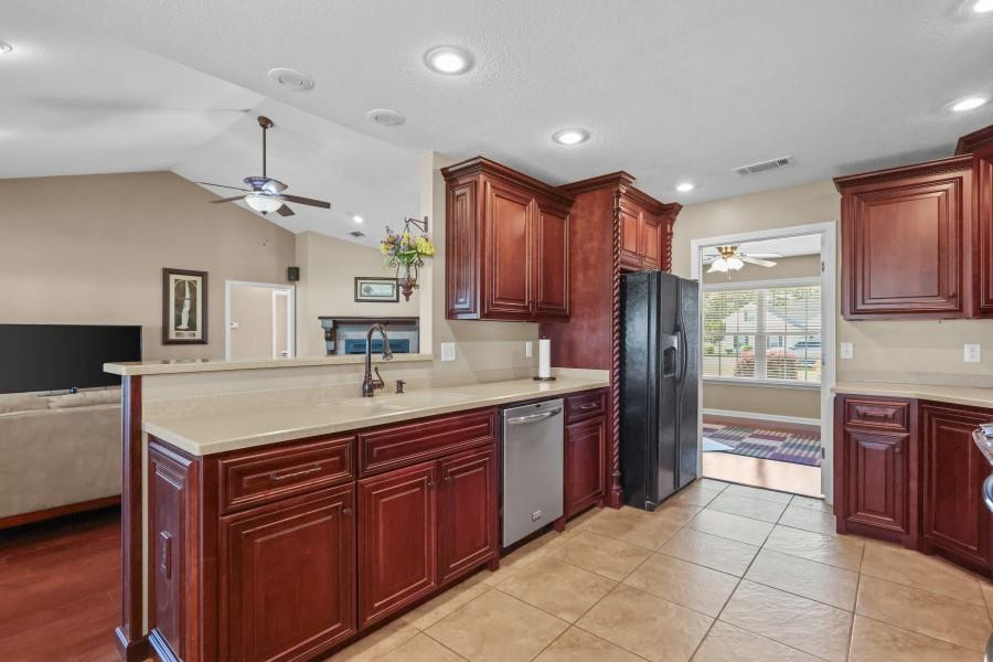 Kitchen with dark wood cabinets, a large sink island, stainless appliances, and tan tile floors.
