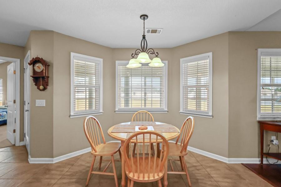 Dining room with a round wooden table, four chairs, multiple windows, and a hanging light.