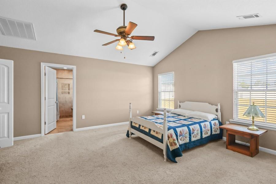 Bedroom with a white bed and blue patchwork quilt, ceiling fan, and doorway to a tiled bathroom.
