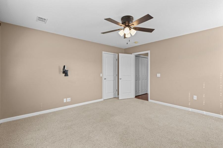 Empty bedroom with beige walls, carpet, and white closet doors.