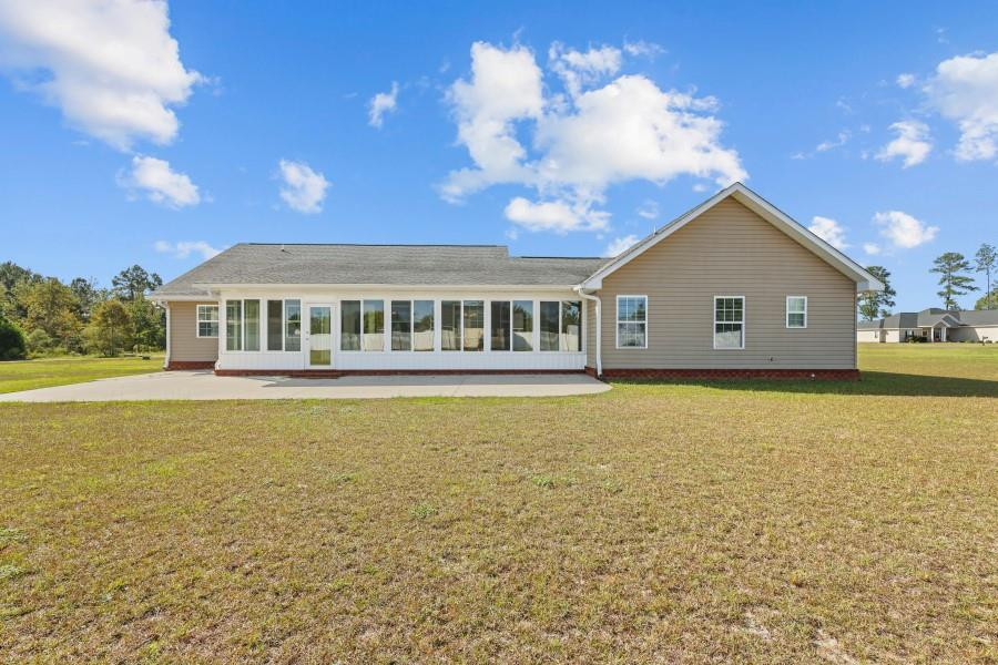 Rear exterior of a beige single-story home with a long enclosed sunroom and broad lawn.