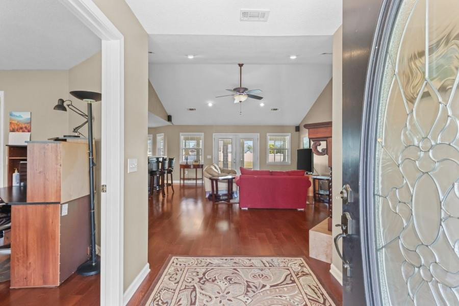 Entryway opening to a living room with reddish hardwood floors, a red sofa, and a decorative glass front door.