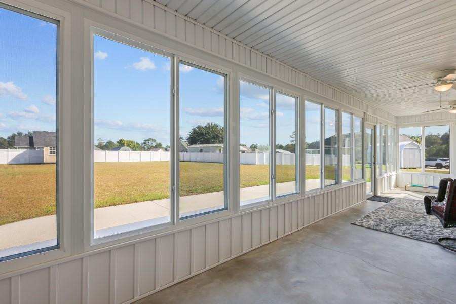 Enclosed sunroom with large windows overlooking a grassy, fenced backyard.