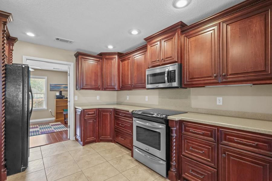 Kitchen with dark wood cabinets, stainless steel appliances, and tan tile flooring.