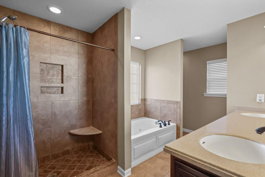 Bathroom with a tiled walk-in shower, blue curtain, separate soaking tub, and beige vanity countertop.