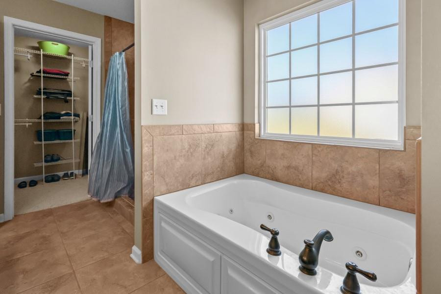 Bathroom with a white jetted soaking tub, tan tile, and a wide gridded window.