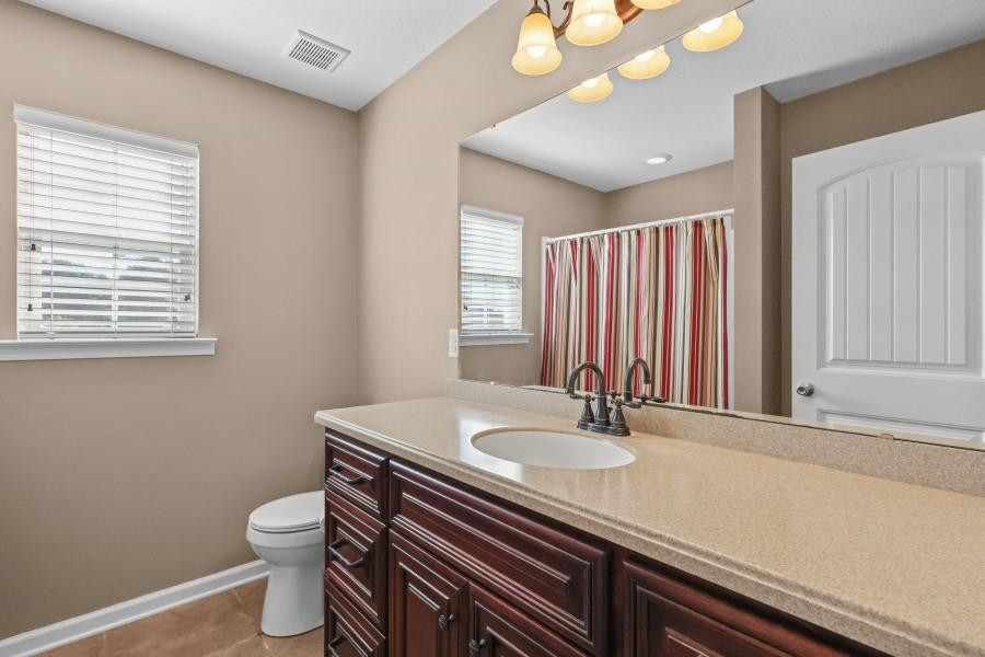 Bathroom with a dark wood double vanity, pale countertop, and striped shower curtain.
