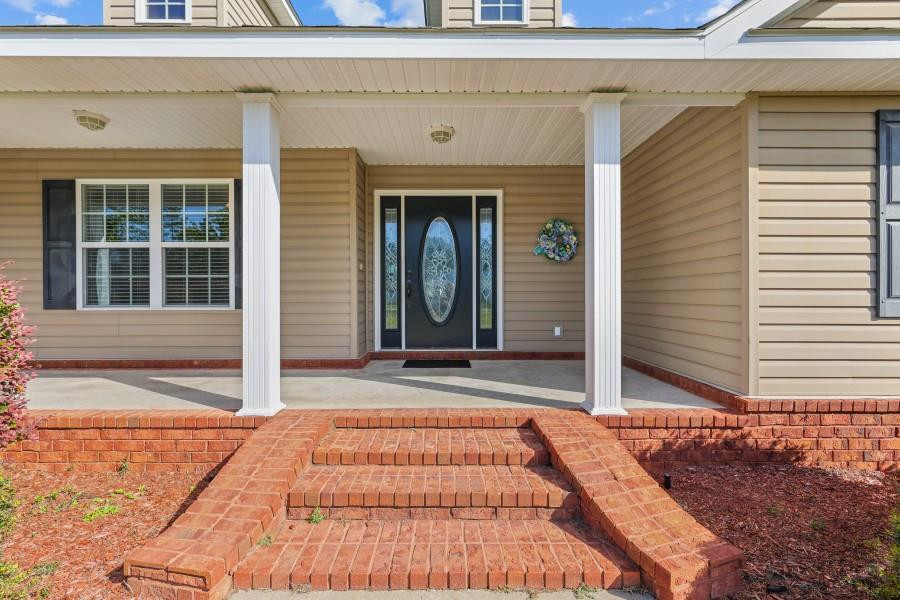 Home’s covered front porch with white columns, decorative glass door, and brick steps.