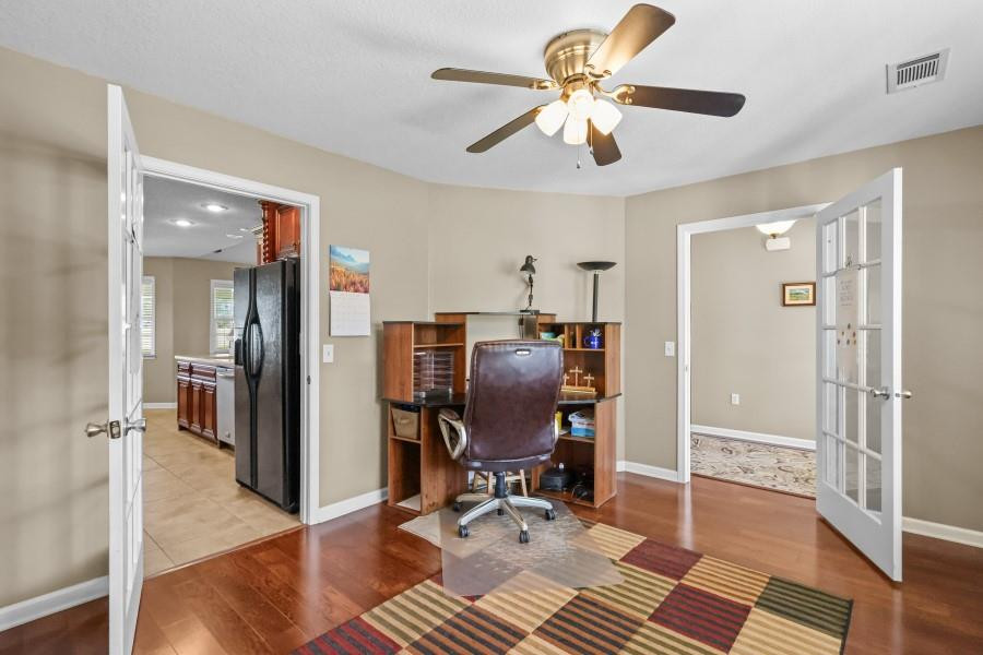 Furnished home office with a wooden desk, leather chair, ceiling fan, and striped rug.