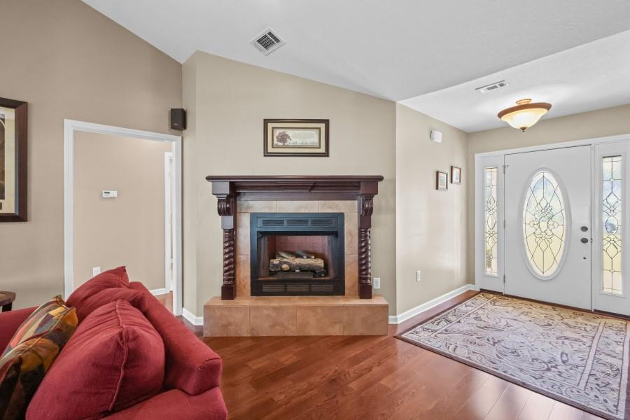 Living room with a carved fireplace, red sofa, hardwood floors, and an oval-glass front door.