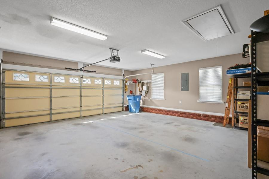Spacious garage with a wide beige door, concrete floor, and storage shelves along the wall.