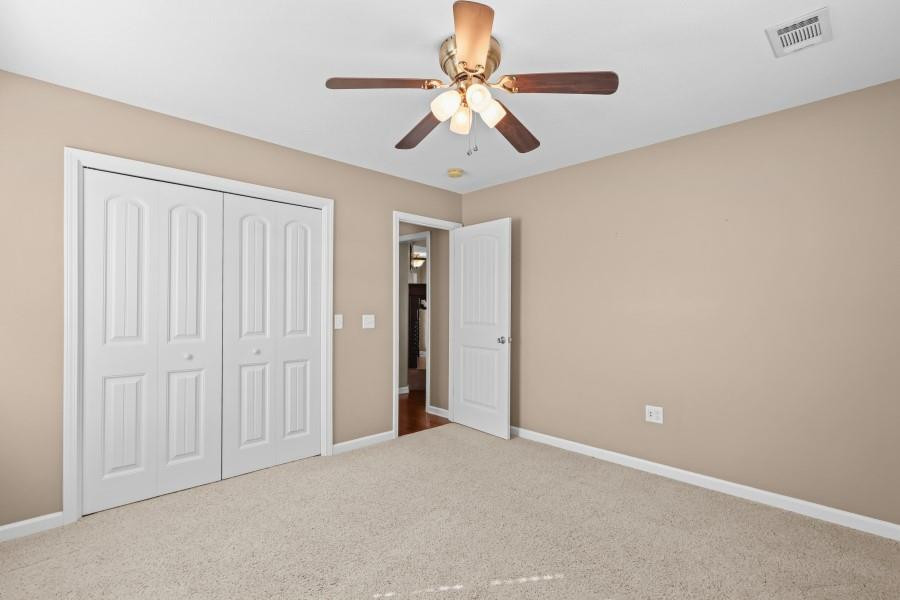 Empty bedroom with beige walls, light carpet, white closet doors, and a ceiling fan.