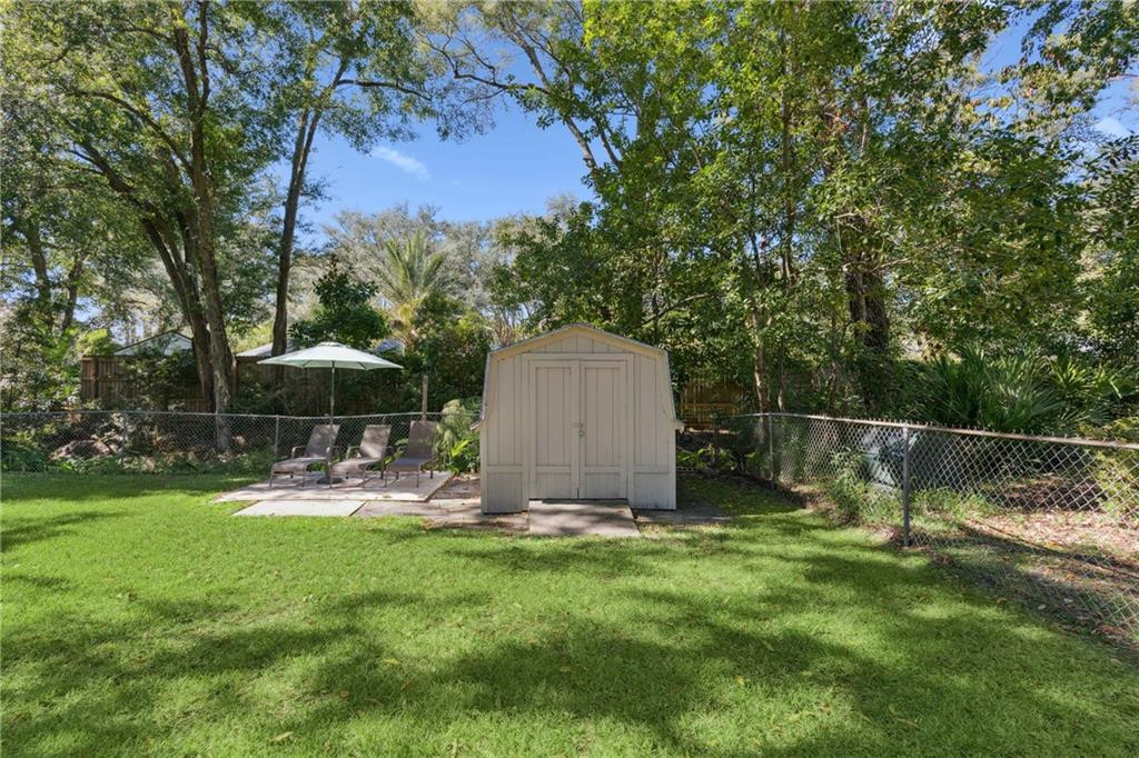 Backyard with a storage shed and patio lounge chairs beneath an umbrella.
