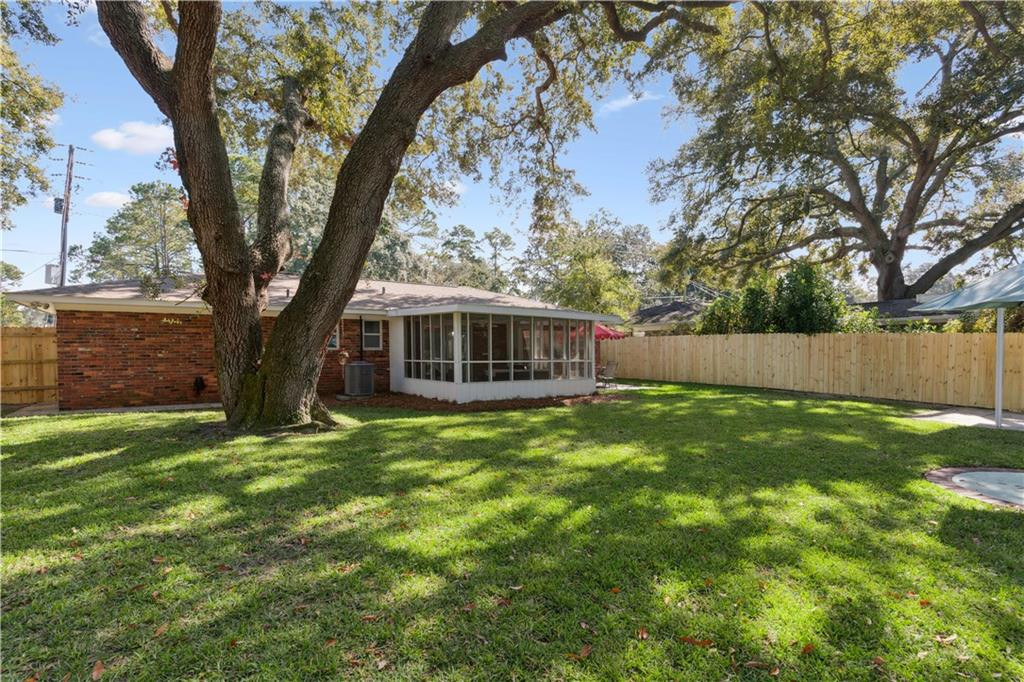 Brick home with a screened porch behind a fenced, oak-shaded lawn.