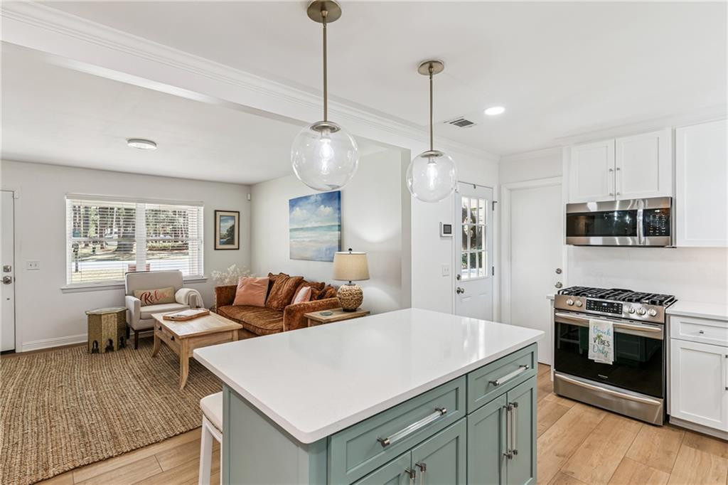 Open-plan kitchen and living area with a pale green island, stainless steel appliances, and brown sofa.