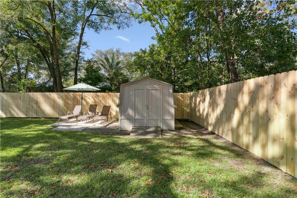 Fenced backyard with a gray shed and lounge chairs beneath a patio umbrella.