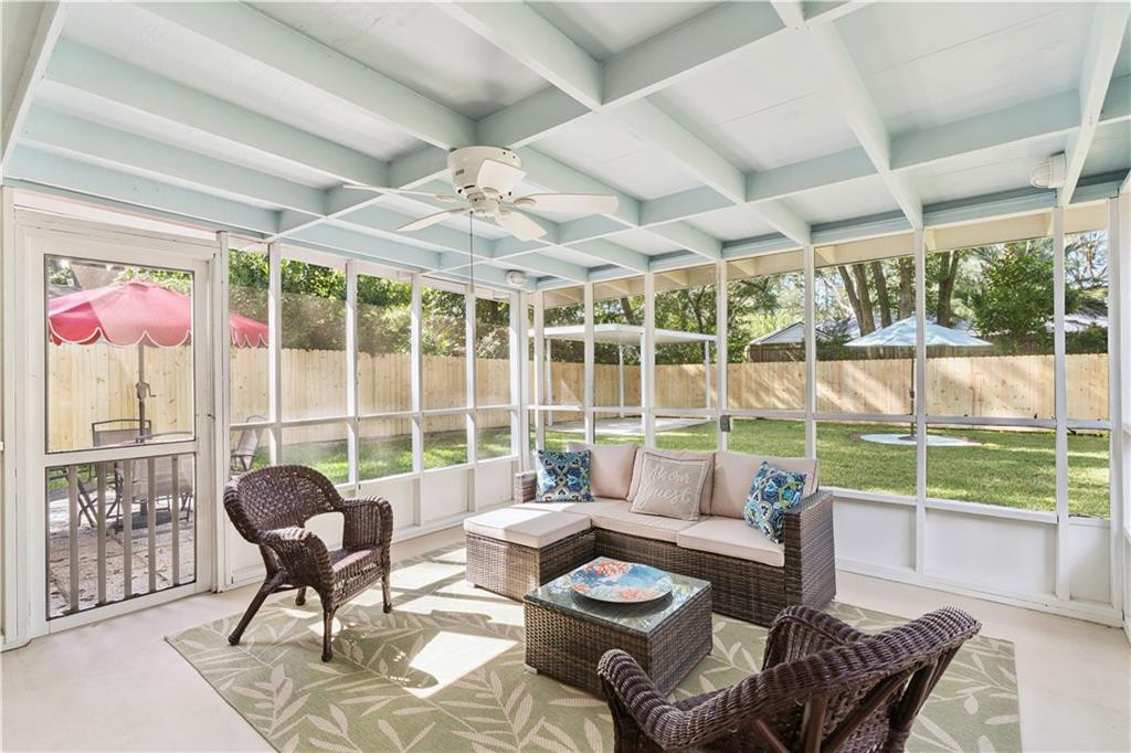 Furnished screened porch with wicker seating, a pale blue beam ceiling, and views of a fenced backyard.