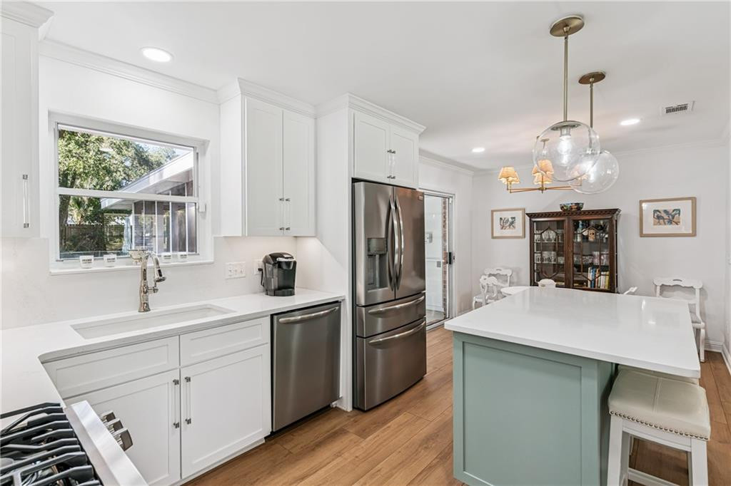 Bright white kitchen with a mint-green island, stainless steel appliances, and warm wood floors.