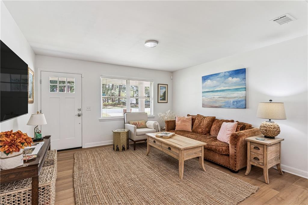 Living room with a brown sofa, woven rug, light wood coffee table, and beach-themed wall art.