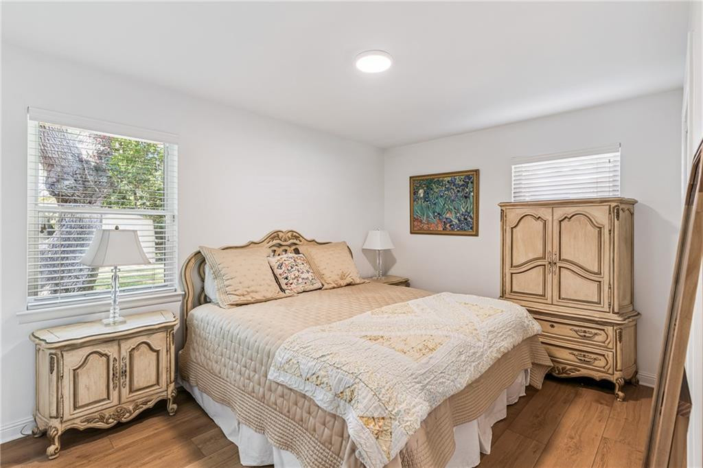 Bedroom with cream bedding, ornate light-wood furniture, hardwood floors, and windows overlooking trees.