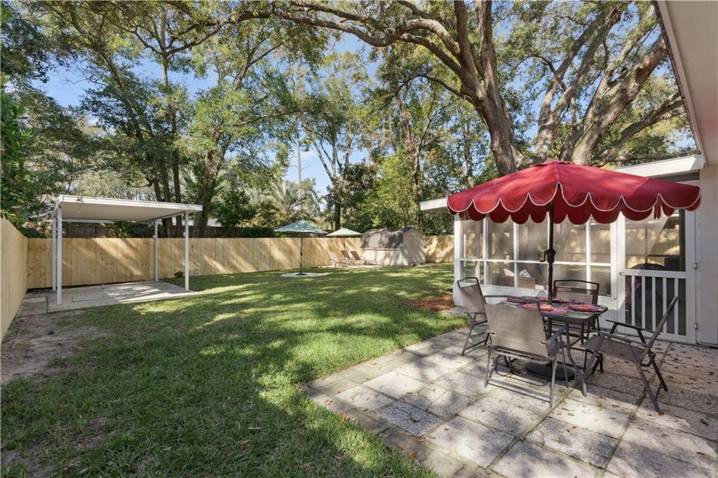 Fenced backyard with a paved patio, red awning, outdoor dining set, and mature trees.