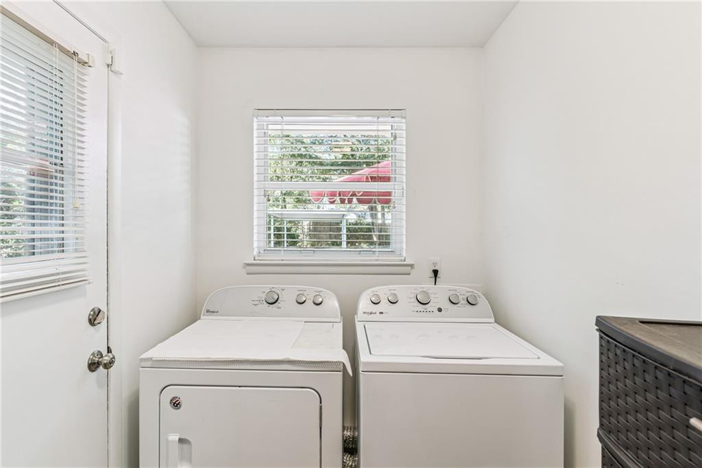 Laundry room with a white washer and dryer beneath a window with blinds.