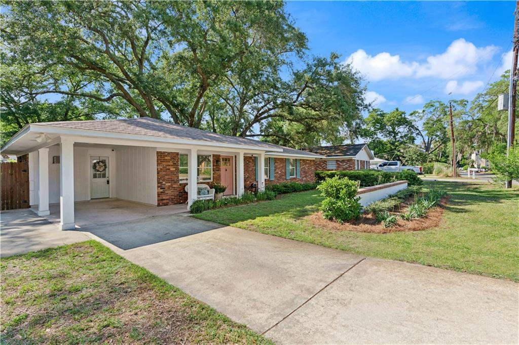 Single-story brick ranch home with a covered carport, broad driveway, and mature trees.