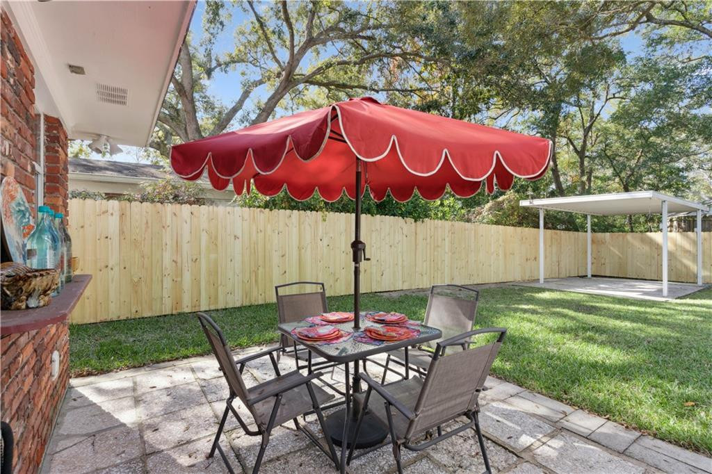 Backyard patio with outdoor dining set beneath a red umbrella and a wooden privacy fence.