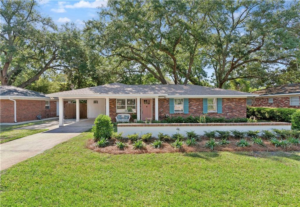 Single-story brick home with blue shutters, covered carport, and mature oak trees.