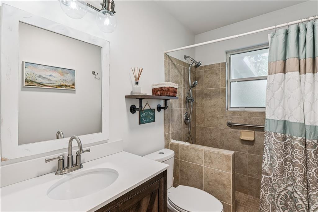 Bathroom with a white vanity and tan tiled shower behind a patterned curtain.