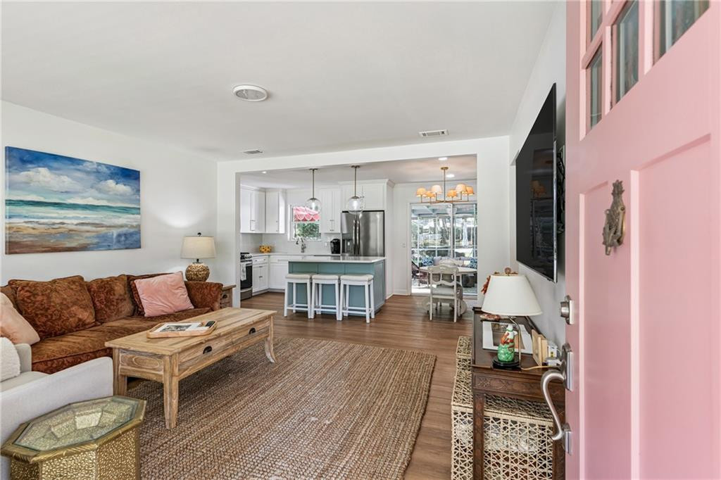 Living room opening to a white kitchen with a teal island, brown sectional, and pink front door.