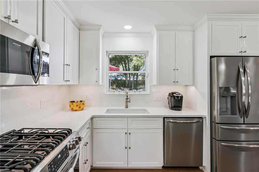 Kitchen with white cabinetry, stainless-steel appliances, and a sink beneath a window overlooking trees.