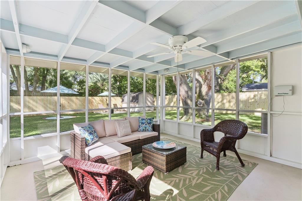 Screened porch with wicker seating, a white beamed ceiling, and views of a leafy garden.