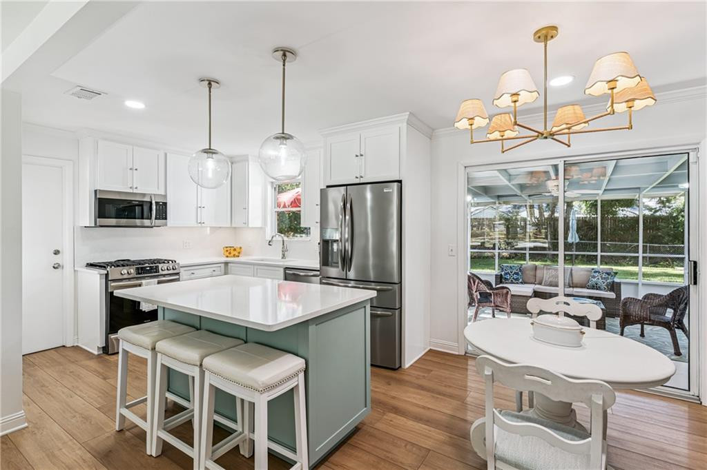 Kitchen with a pale green island, stainless steel appliances, and dining area beside patio doors.