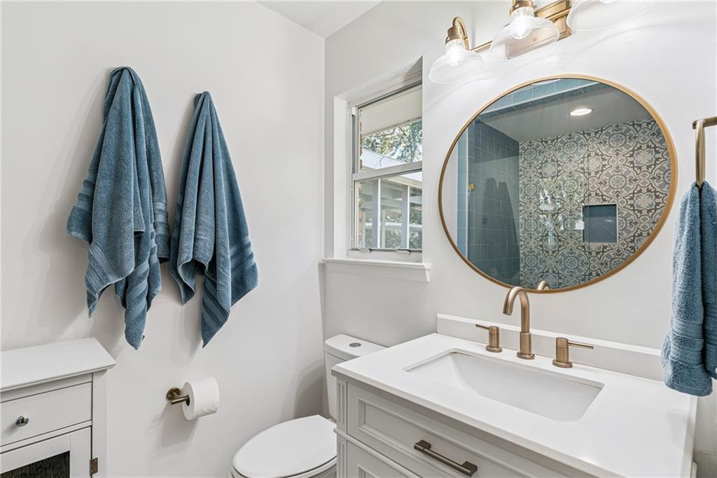 Bathroom with a brass-framed round mirror, blue towels, and patterned shower tile.