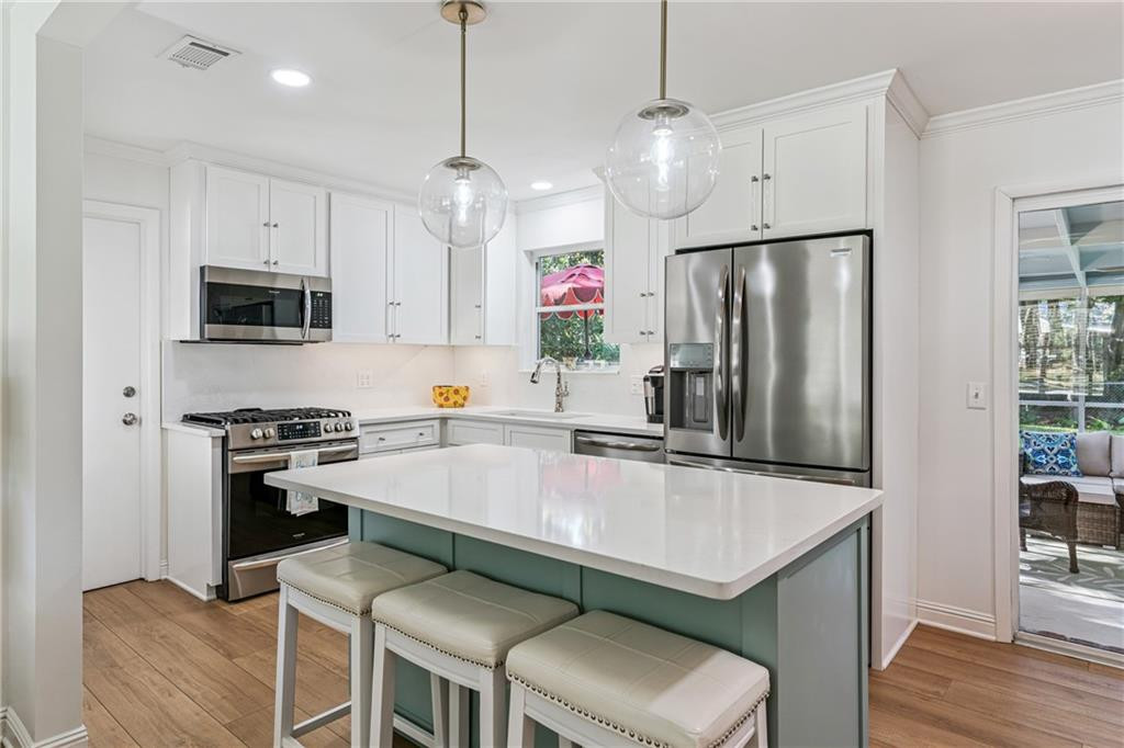 Bright kitchen with a teal-based island, three stools, white cabinets, and stainless steel appliances.