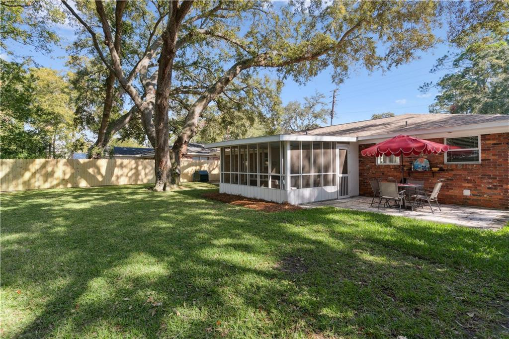 Brick home backyard with screened porch, patio seating, broad lawn, and mature shade tree.