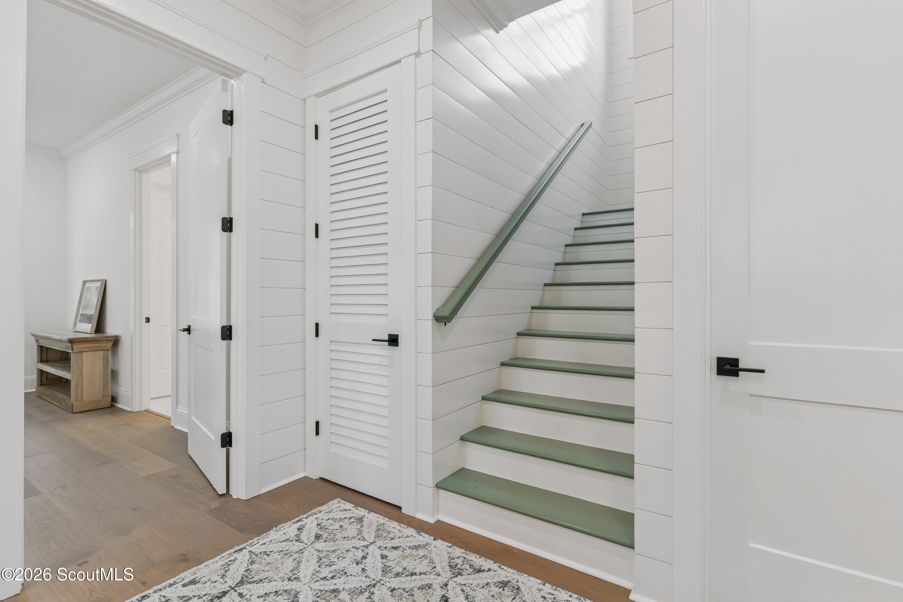 Interior staircase with muted green treads and handrail beside a white louvered door.