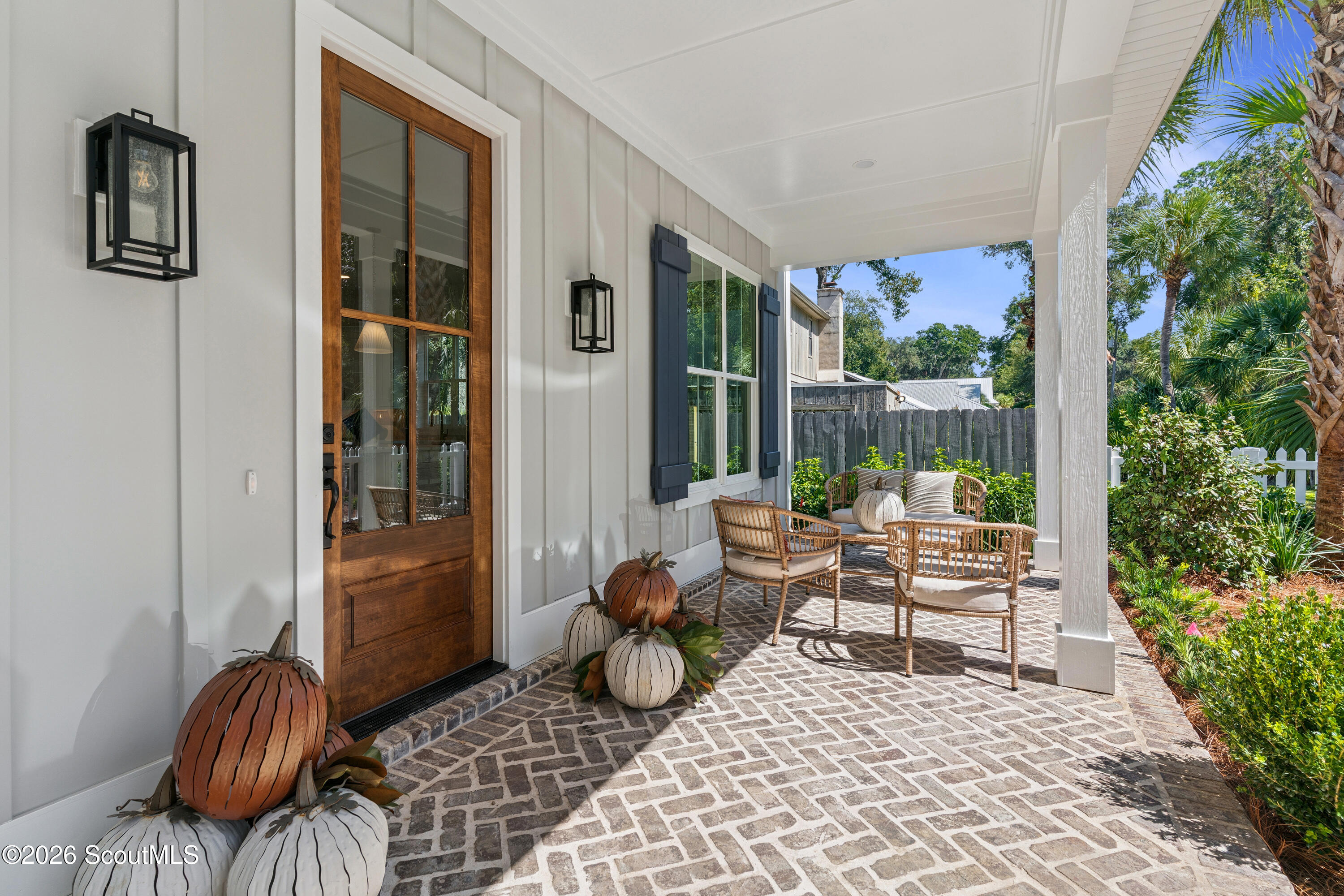 Covered front porch with wicker seating, brick pavers, a wood entry door, and decorative pumpkins.