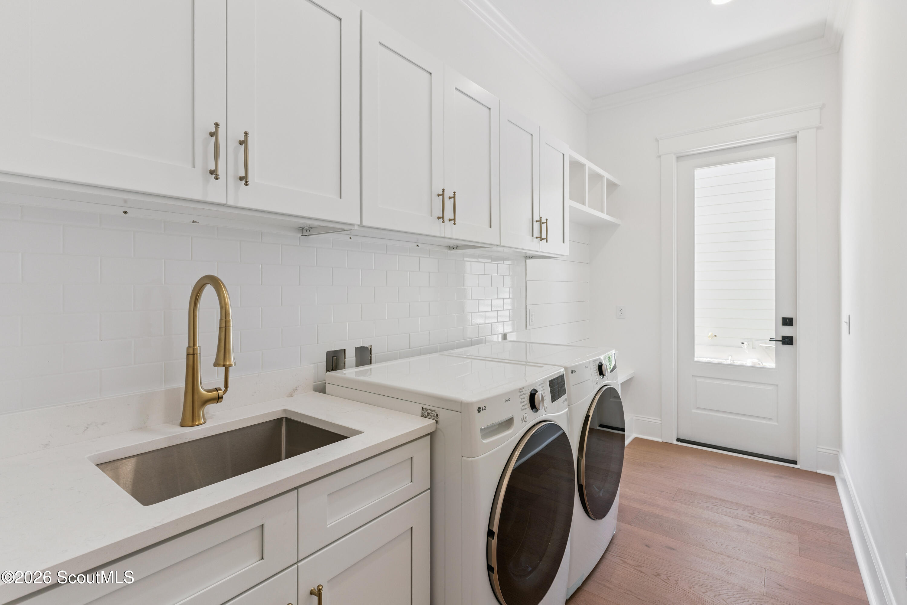 Laundry room with white cabinetry, a brass-faucet sink, and front-loading washer and dryer.